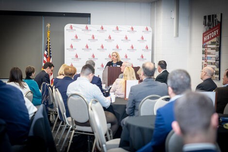 A woman stands at a podium talking to a crowd sitting in front of her