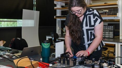Ava Bickford stands over a table adjusting optical equipment.