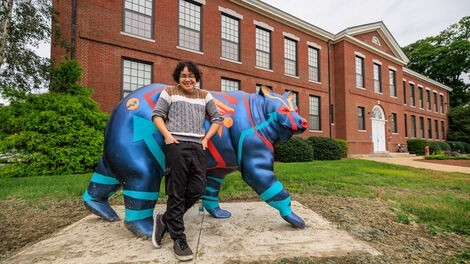 A young man stands in front of a blue painted bear 