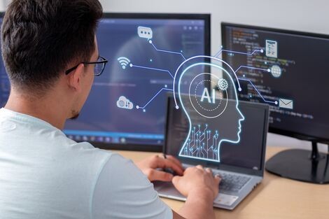 A man sits in front of a computer screen that says AI