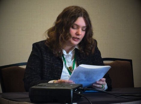 A woman sits and reads from a piece of paper