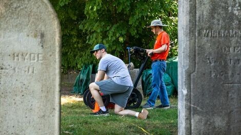Framed by two gravestones, a professor and student work with ground-penetrating radar.