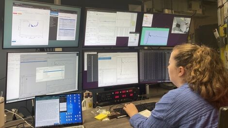 Shannon McLaughlin types while sitting in front of a large display of monitors.