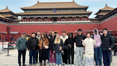 A large group of students stands next to a building in the Forbidden City.