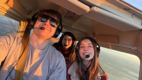 Three people fly in a small plane while wearing headsets.