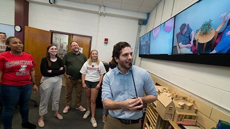 A professor and students watch a mock counseling session on a video monitor.