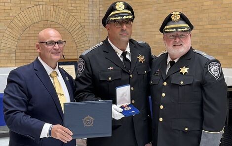 Three men stand together holding an award 