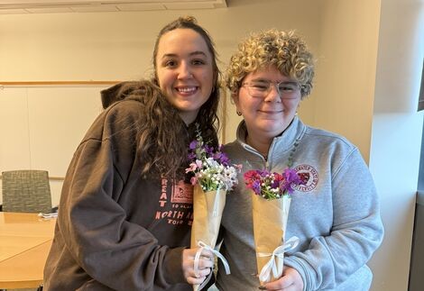 Two women stand together smiling and holding flowers 