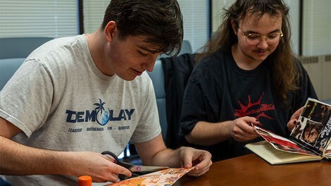 Two students make scrapbooks while sitting at a table.