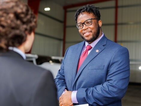 A man wearing glasses smiles as he listens to another man talk