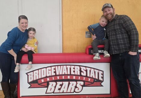 A woman, man and two small children stand in front of a sign that reads Bridgewater State University 