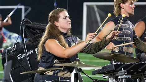 Delaney Hughes plays percussion instruments on a football field.