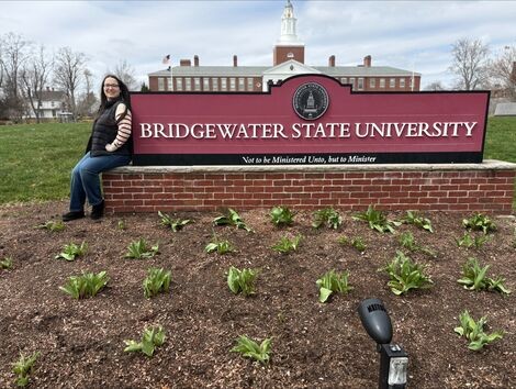 A woman leans on a Bridgewater State University sign 