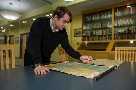 A man stands over a desk looking at a map