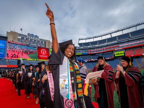 a woman in a cap and gown raises her hand to the sky and smiles