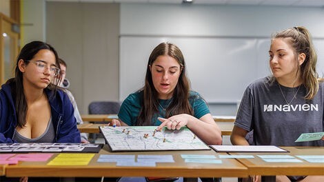 Three students look at a display featuring a map.