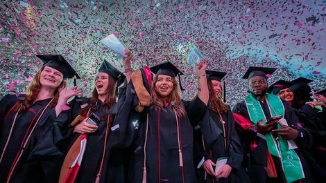 Graduates cheer and raise their hands as confetti rains down.