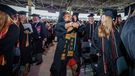 A graduate dances in the aisle as others cheer her on enthusiastically. 