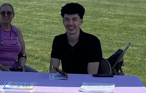 A young man sits at a table and smiles
