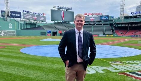 A man stands wearing a suit at a baseball park