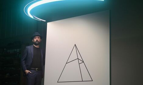 A man stands next to a white canvas with a triangle on it with a blue light above him