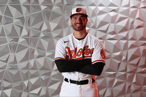 A man stands with his arms crossed wearing a baseball uniform