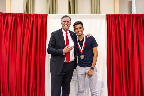 Two men stand together smiling in front of a red curtain 