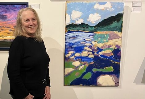 A woman stands smiling next to a piece of artwork 