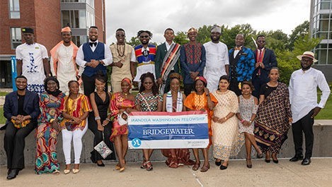 Mandela fellows pose for a group photo while wearing formal outfits and holding a fellowship banner.