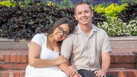 Maddie Monagle and Jonny Matthews sit close together on an outdoor bench,