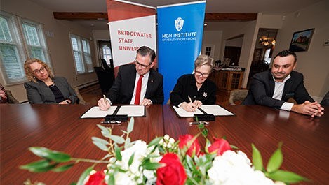 BSU and IHP leaders sign an agreement while sitting at a large tables with flowers in front of them.