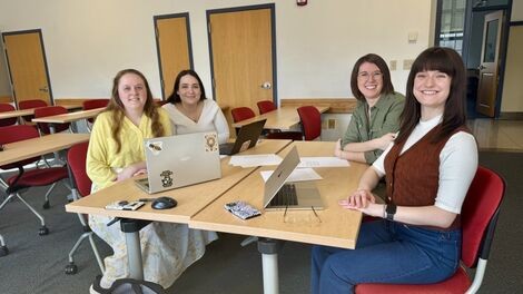 Four people smile while sitting at a table in a classroom.