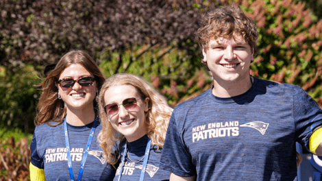 Three people stand together smiling wearing Patriots tshirts 