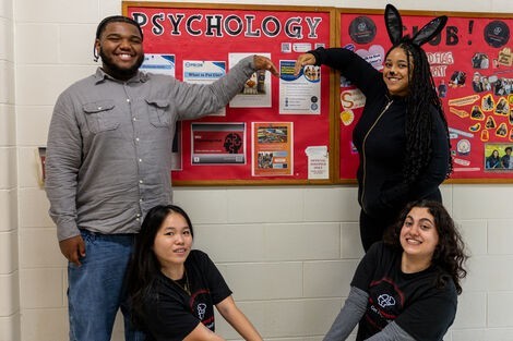 A group of people smile and stand next to a psychology sign 