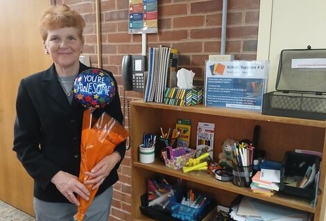 A woman stands holding flowers next to a bookshelf