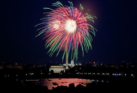 Red and green fireworks burst in the sky over Washington, DC, with the Capitol, Washington Monument, and Lincoln Memorial in view