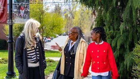 Three people walk along a path while talking with plants, grass and trees around them.