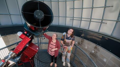 Two people look up while using a telescope inside a large dome.