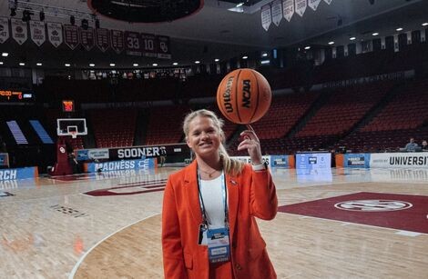 A woman wears a red suit and twirls a basketball on her finger 