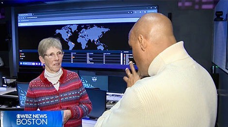 A journalist interviews a professor in the cyber range with a large digital display in the background showing a map of the world.