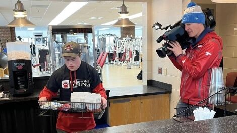 A videographer records a student working at a food stand.