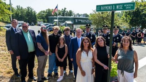 A group of people stands next to a sign for Raymond Wise Drive