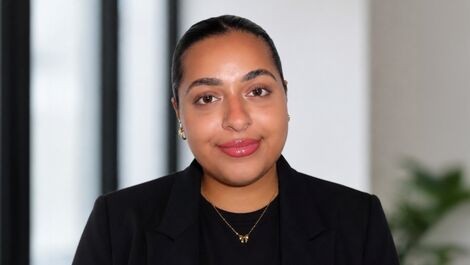Headshot of Zainab standing in front of windows and a wall.