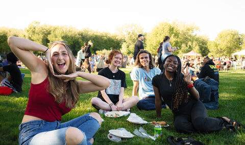 Four students pose for the camera while sitting on the lawn at the Welcome Back BBQ