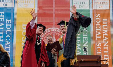 A BSU student dressed in Native American attire receives his diploma. He and President Fred Clark wave to the crowd.