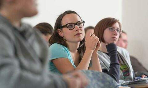 student sitting in desks in a BSU Special Education class focused on 2 female students listening attentively to the professo