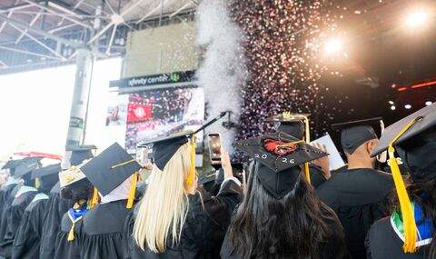 Undergraduate grads hold up their phones while looking toward the Commencement stage where confetti is projecting from
