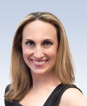 Danielle Bazinet smiling with long dirty blonde hair parted in the middle wearing a square neck black top with one sleeve