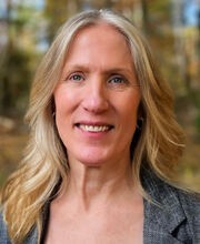 Dr. Darcy Boellstorff smiling with long blonde hair and wearing a gray blazer over a black top
