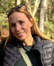 Kristen Buchanan smiling with long light brown hair and wearing a black vest over a long sleeve green top
